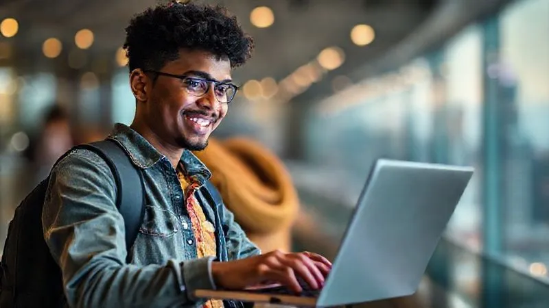 A photorealistic, professional photography, 8K image of a young, diverse nomadic student enthusiastically presenting a digital project on a laptop, with a vibrant cityscape or natural landscape blurred in the background, conveying a sense of global connection and achievement. Cinematic lighting, sharp focus on the student's face and screen, depth of field. Shot on a high-end DSLR.