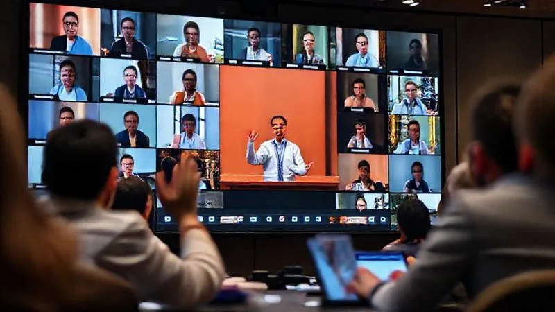 A screen showing a lively virtual conference with multiple video feeds of diverse participants, some raising hands, others typing in a chat window. The main speaker is visible in a large frame, presenting engagingly. The overall atmosphere is collaborative and high-tech. Photorealistic, professional photography, 8K, cinematic lighting, sharp focus on the screen, depth of field, shot on a high-end DSLR.