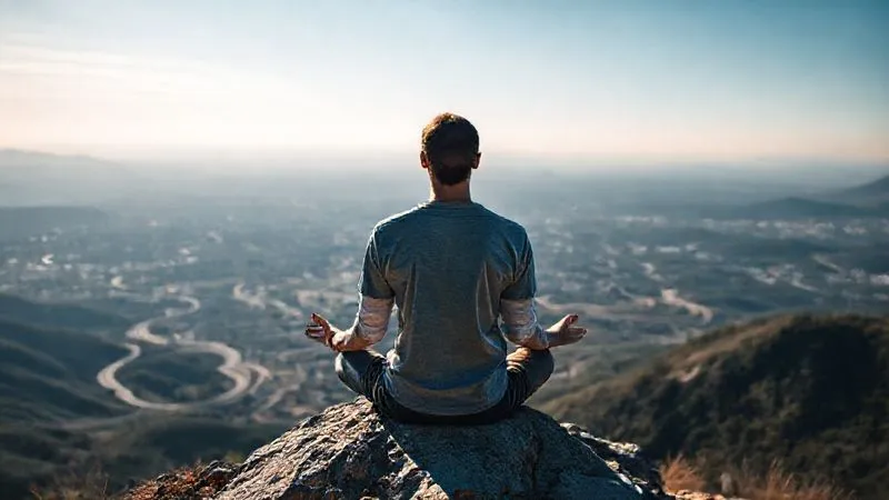 A photorealistic image of a person meditating calmly on a mountaintop overlooking a vast, complex landscape of winding roads and distant cities, symbolizing overcoming project complexities. The person has a serene expression. Cinematic lighting, sharp focus on the person, depth of field blurring the landscape, 8K hyper-detailed, professional photography, emotionally resonant.