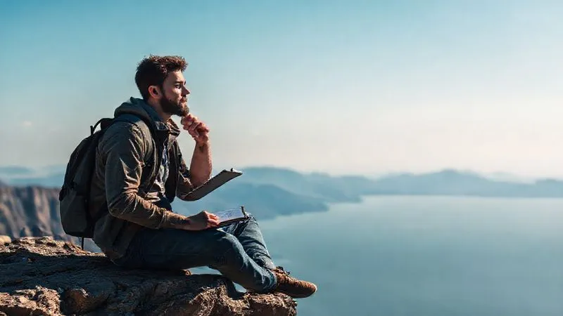 Photorealistic image of a thoughtful digital nomad sitting on a cliff overlooking a vast landscape, holding a journal and a pen, reflecting deeply on their career path. The sky is clear, suggesting clarity of thought. Professional photography, 8K, cinematic lighting, sharp focus on the nomad, depth of field blurring the distant mountains and ocean, shot on a high-end DSLR.