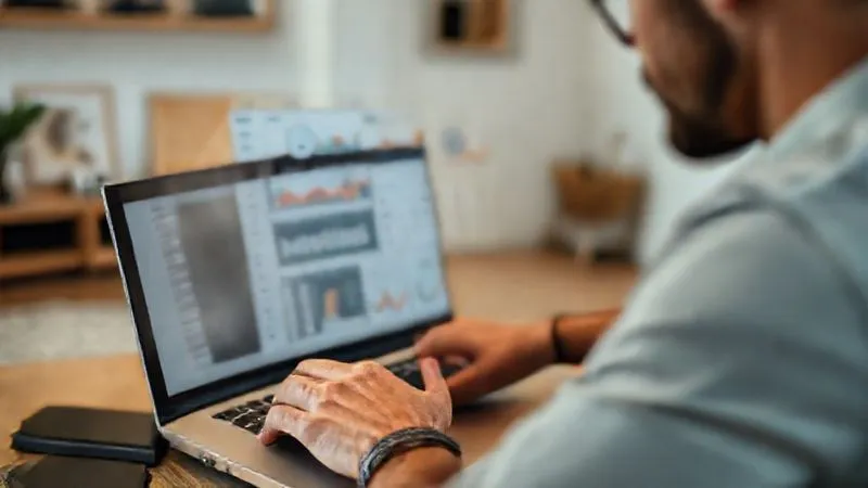 A photorealistic image of a digital nomad, male, focused on a laptop screen displaying a clean, intuitive financial dashboard with various charts and graphs. His fingers are hovering over a trackpad, suggesting active organization. In the background, a minimalist, modern apartment with travel souvenirs subtly placed. Cinematic lighting, sharp focus on the man and screen, depth of field blurring the background, 8K hyper-detailed, shot on a high-end DSLR.